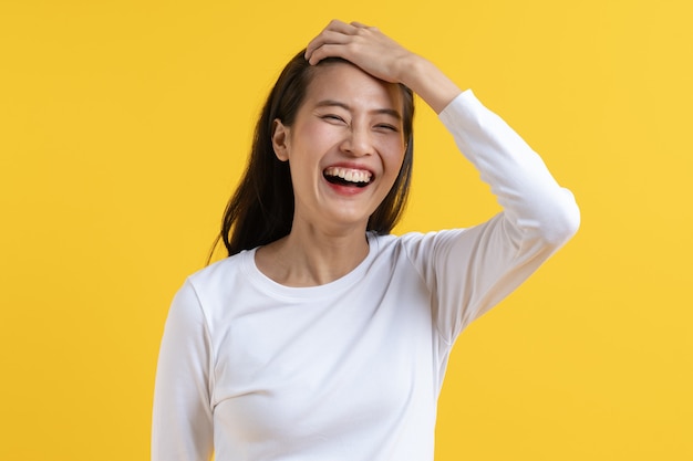 Schüchterne asiatische junge Frau, die lokalisiert auf gelbem Hintergrund lacht