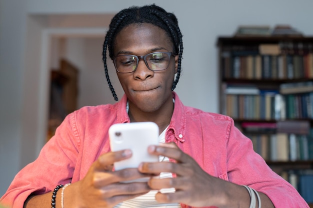 Schüchterner introvertierter Afroamerikaner, der am Telefon chattet und mit Mädchen über das Internet flirtet, sitzt am Tisch