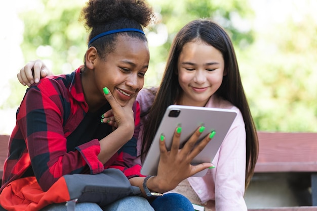 Schüler benutzen Tablet mit Freund und schauen sich Tablet im Schulpark an