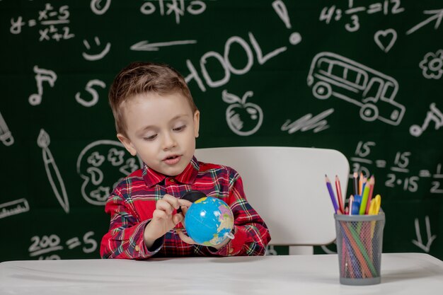 Schüler, der einen runden Globus in den Händen einer mit einer Tafel gemalten Tafel hält