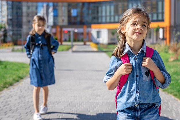 Schüler der Grundschule. Mädchen mit Rucksäcken in der Nähe des Gebäudes im Freien. Beginn des Unterrichts. Erster Herbsttag.