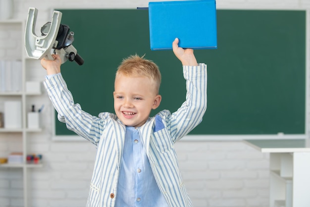 Schüler des Schulkindes lernen Unterricht, der am Schreibtisch sitzt und Schüler der Früherziehung mit Mikroskop studiert