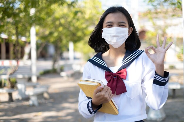 Schüler halten Buch und tragen Maske in Schuluniform