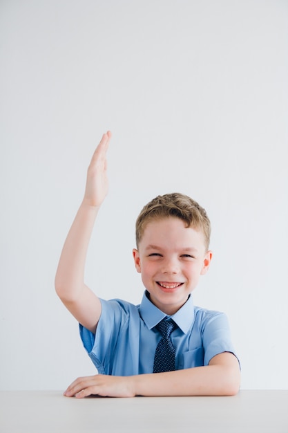 Schüler in Schuluniform hebt seine Hand am Schreibtisch