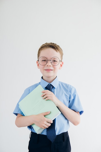 Schüler in Schuluniform und Brille hält einen Stapel Notizbücher in den Händen