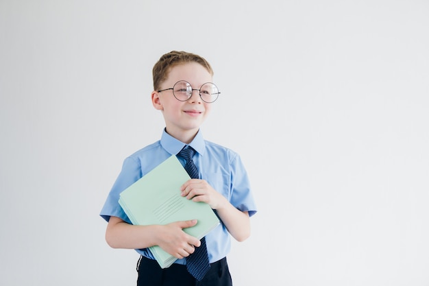 Schüler in Schuluniform und Brille hält einen Stapel Notizbücher in den Händen