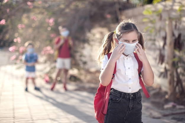 Schüler mit medizinischer Maske im Gesicht und Rucksäcken im Freien. Ausbildung während der Coronavirus-Zeit. Kinder und Gesundheitswesen. Zurück zur Schule.