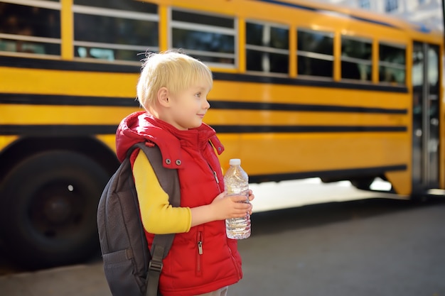 Schüler mit Schultasche und Flasche Wasser nahe gelbem Schulbus