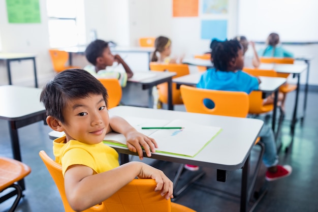 Schüler sitzt an seinem Schreibtisch und schaut in die Kamera im Klassenzimmer