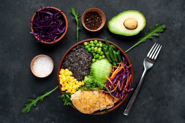 Schüssel Buddha.Quinoa, Hühnerbrust, Rucola, Avocado, Rotkohl, Karotte, grüne Erbsen, Mais, Tomate, grüne Bohnen in einem weißen Teller.