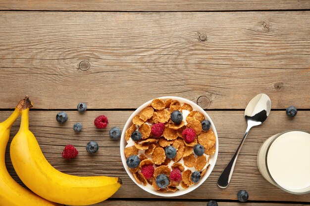 Schüssel Cornflakes und frische Beeren und frische Früchte auf grauem Holzhintergrund. Ansicht von oben.