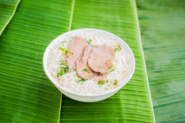 Schüssel der traditionellen vietnamesischen rindfleischsuppe pho bo auf bananenblatthintergrund.