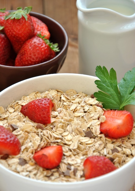 Schüssel Getreide mit Milch und Erdbeeren auf Holztisch