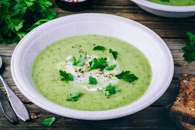 Schüssel grüne Zucchinicremesuppe mit frischer Petersilie auf hölzernem Hintergrund Beschneidungspfad eingeschlossen