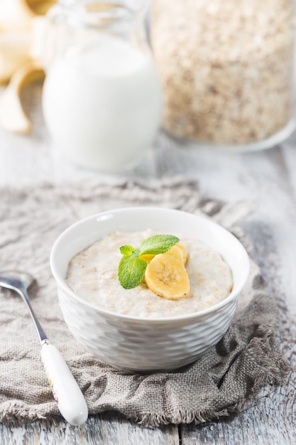 Schüssel Haferflockenbrei mit Banane auf weißem rustikalem Holztisch, gesundes Frühstück, Diätkost.