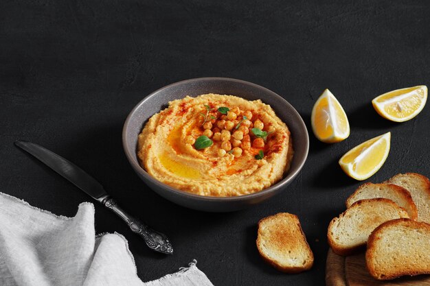 Schüssel Hummus mit Paprika auf dunklem Tisch mit Zitronen- und Brotkopierraum