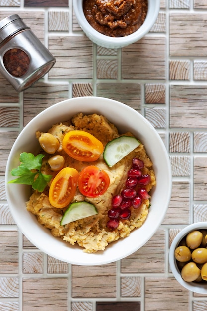 Schüssel Hummus, traditionelles jüdisches, arabisches, nahöstliches Essen aus Kichererbsen mit Dip-Tahini und Oliven auf Keramikfliesenhintergrund. Nahaufnahme, Draufsicht