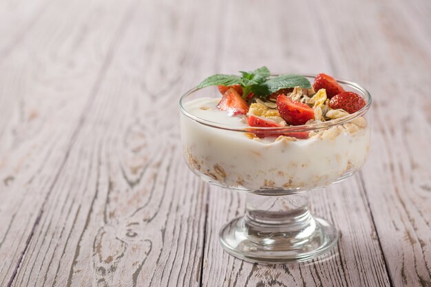 Schüssel Joghurt und Haferflocken mit Erdbeeren auf einem rustikalen Tisch dekoriert.