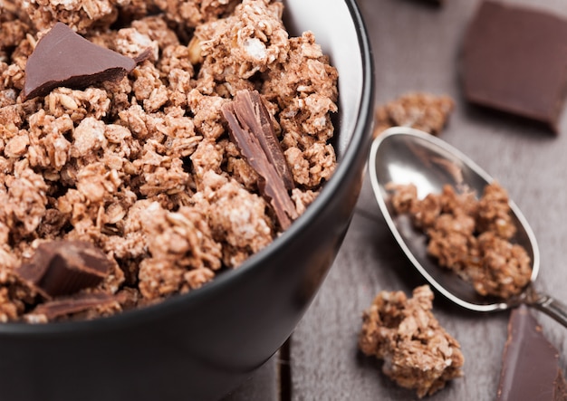 Schüssel mit Bio-Schokoladen-Müsli-Frühstücksflocken auf Holz mit Schokoriegel auf Holz