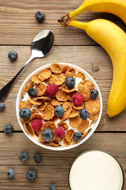 Schüssel mit Cornflakes und frischen Beeren und frischen Früchten auf grauem Hintergrund.