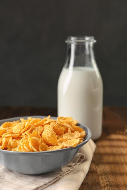 Schüssel mit Cornflakes und Milchflasche auf Holztisch