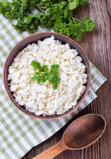 Schüssel mit frischem Hüttenkäse und Holzlöffel auf braunem Holzhintergrund. Draufsicht, flach liegen