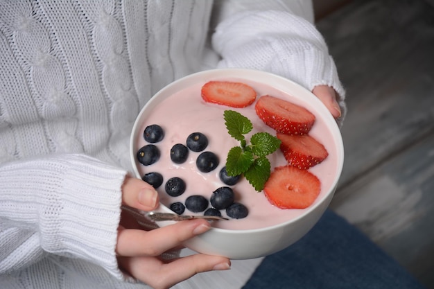 Schüssel mit frischen gemischten Beeren und Joghurt mit frischen Erdbeeren und Heidelbeeren auf dem Bauernhof in den Händen des Mädchens