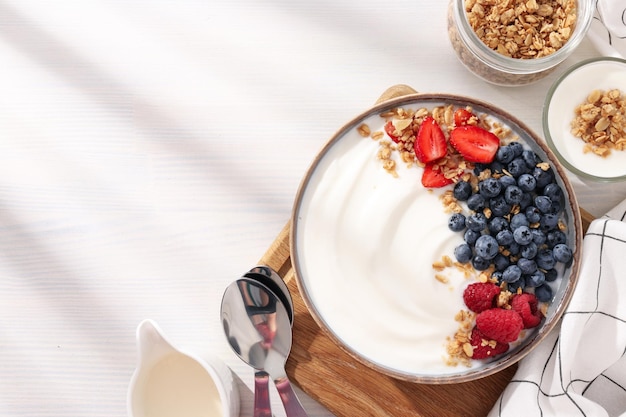 Schüssel mit Joghurt und Beeren an Bord, Glas und Handtuch auf hellem Hintergrund, Platz für Text