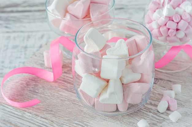 Schüssel mit leckeren Marshmallows und rosa Schleife auf weißem Tisch, Nahaufnahme.