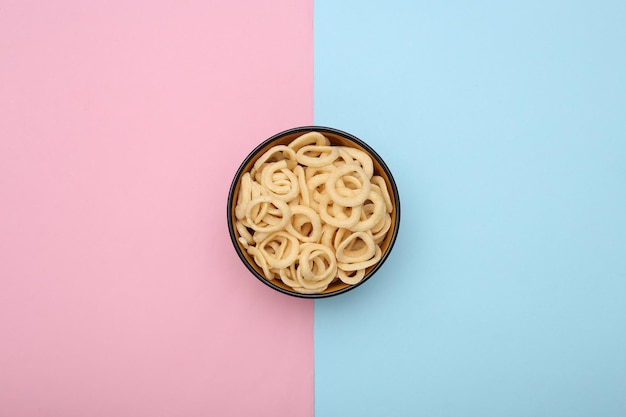 Schüssel mit Maisringen auf blau-rosa Pastellhintergrund. Snacks. Ansicht von oben