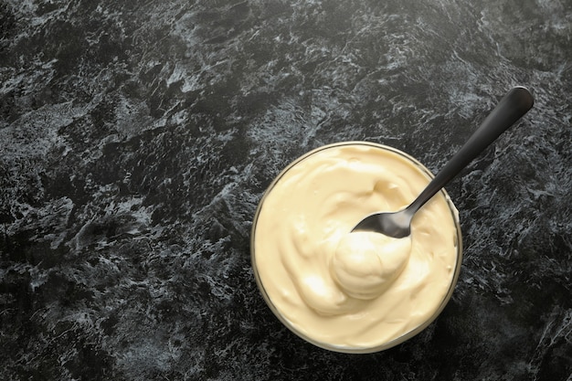 Schüssel mit Mayonnaise und Löffel auf schwarzem rauchigem Hintergrund