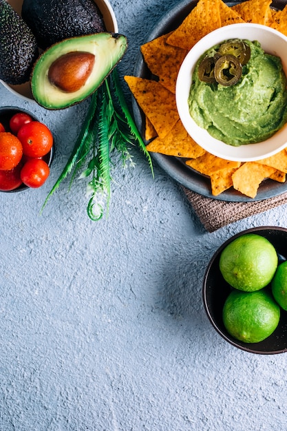 Schüssel mit mexikanischer Guacamole auf Vintage-Holztisch, umgeben von Tomaten, Jalapeños-Paprika, Limetten und Avocados. Copyspace