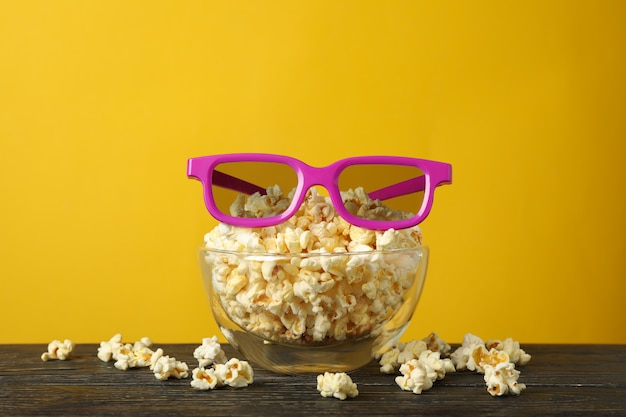 Schüssel mit popcorn und 3d-gläsern auf holztisch. essen zum kino gucken