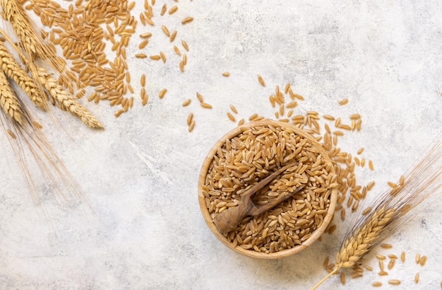 Schüssel mit rohem, trockenem Roggenkorn mit einem Holzlöffel auf weißer Tischplatte