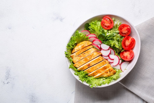 Schüssel mit Salat und in Scheiben geschnittenem Hühnerfilet. Diät-Mittagessen, Keto-Diät, gesundes Essen. Draufsicht auf weißem Hintergrund.