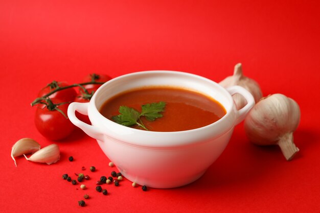 Schüssel mit Tomatensuppe und Zutaten auf rot