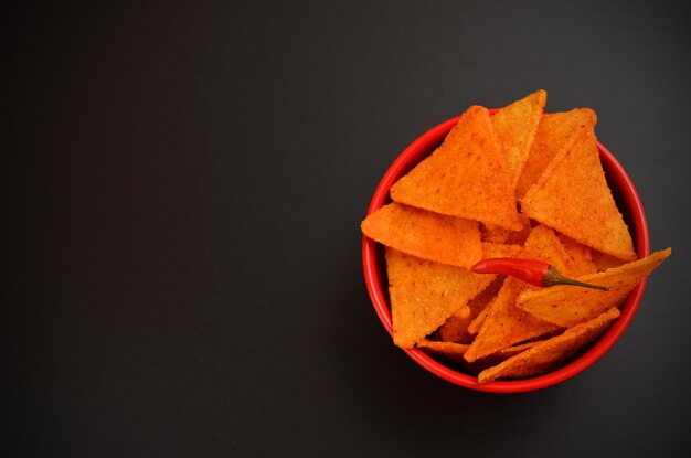 Schüssel mit würzigen Maischips auf dunklem Hintergrund, flach liegender Kopierraum