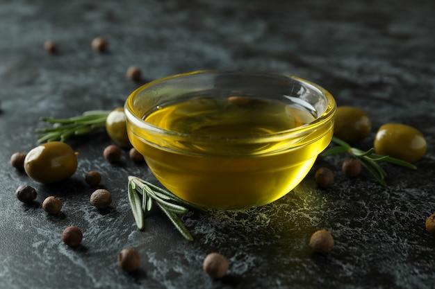 Schüssel Olivenöl, Oliven, Pfeffer und Rosmarin auf schwarzem rauchigem Hintergrund