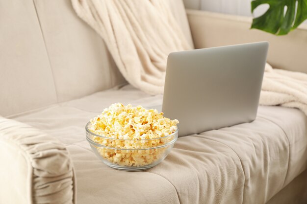 Schüssel Popcorn und Laptop auf Sofa. Filme nach Hause schauen