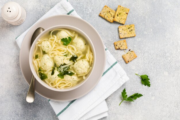 Schüssel traditionelle italienische Suppe mit Hühnerfleischbällchen und Eipaste, Parmesankäse, Petersilie auf grauer Tischwand. Traditionelle italienische Küche. Draufsicht.