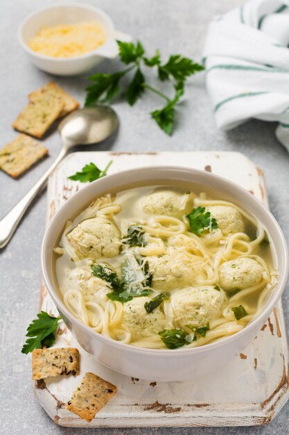 Schüssel traditionelle italienische Suppe mit Hühnerfleischbällchen und Eipaste, Parmesankäse, Petersilie auf grauer Tischwand. Traditionelle italienische Küche. Draufsicht.