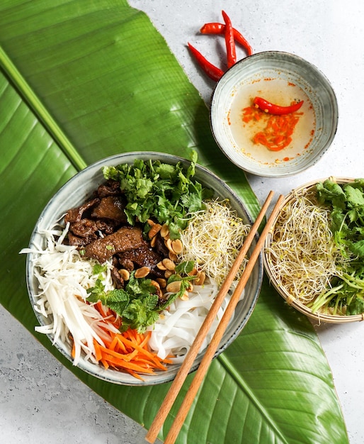 Schüssel traditioneller vietnamesischer Salat Bun Bo Nam Bo mit Rinderreisnudeln, frischen Kräutern, eingelegtem Gemüse und Fischsauce