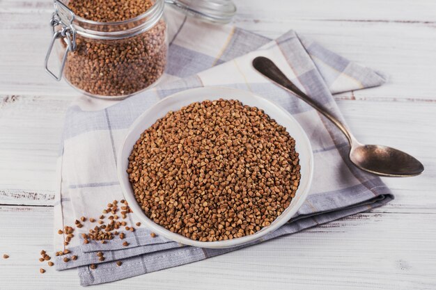 Schüssel trockene rohe Buchweizengrütze auf einem weißen Holztisch. Buchweizenbrei-Konzept kochen.