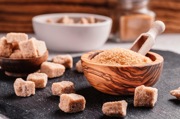 Foto schüssel und schaufel mit sand und klumpen brauner zucker auf holzhintergrund brauner zuckerwürfel machen sie ungesunde ernährung, fettleibigkeit, diabetes, zahnpflege und vieles mehr