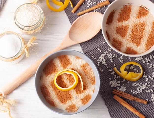 Schüsseln Milchreis mit Reis auf dem Tisch verstreut Zitronenscheiben einen Holzlöffel und Zimtstangen