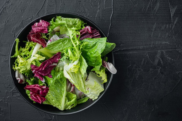 Schüsseln mit gemischten frischen Salatblättern, auf schwarzem Tisch, Draufsicht flach liegen