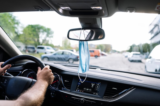 Schützende Gesichtsmaske, die vom Rückspiegel des Autos hängt