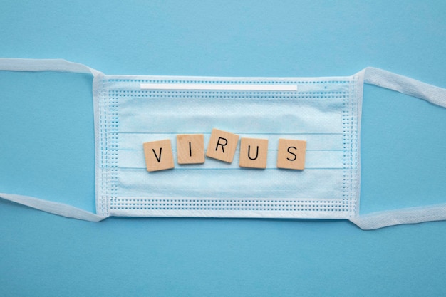 Schützende medizinische Gesichtsmaske mit dem Wort Virus auf blauem Hintergrund