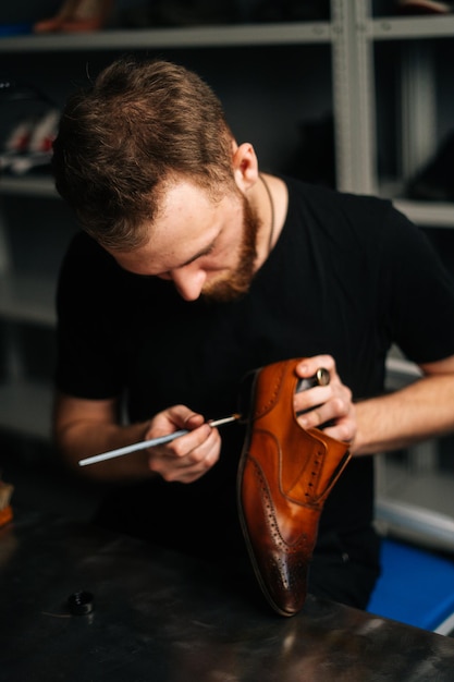 Schuhmacher beim Bemalen von Absatz und Sohle von hellbraunen Lederschuhen mit Pinsel während Restaurierungsarbeiten