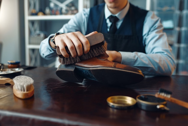 Schuhmacher wischt schwarze Schuhcreme ab, Reparaturservice für Schuhe. Handwerkskunst, Schuhmacherwerkstatt, Meisterarbeiten mit Stiefeln, Schusterladen